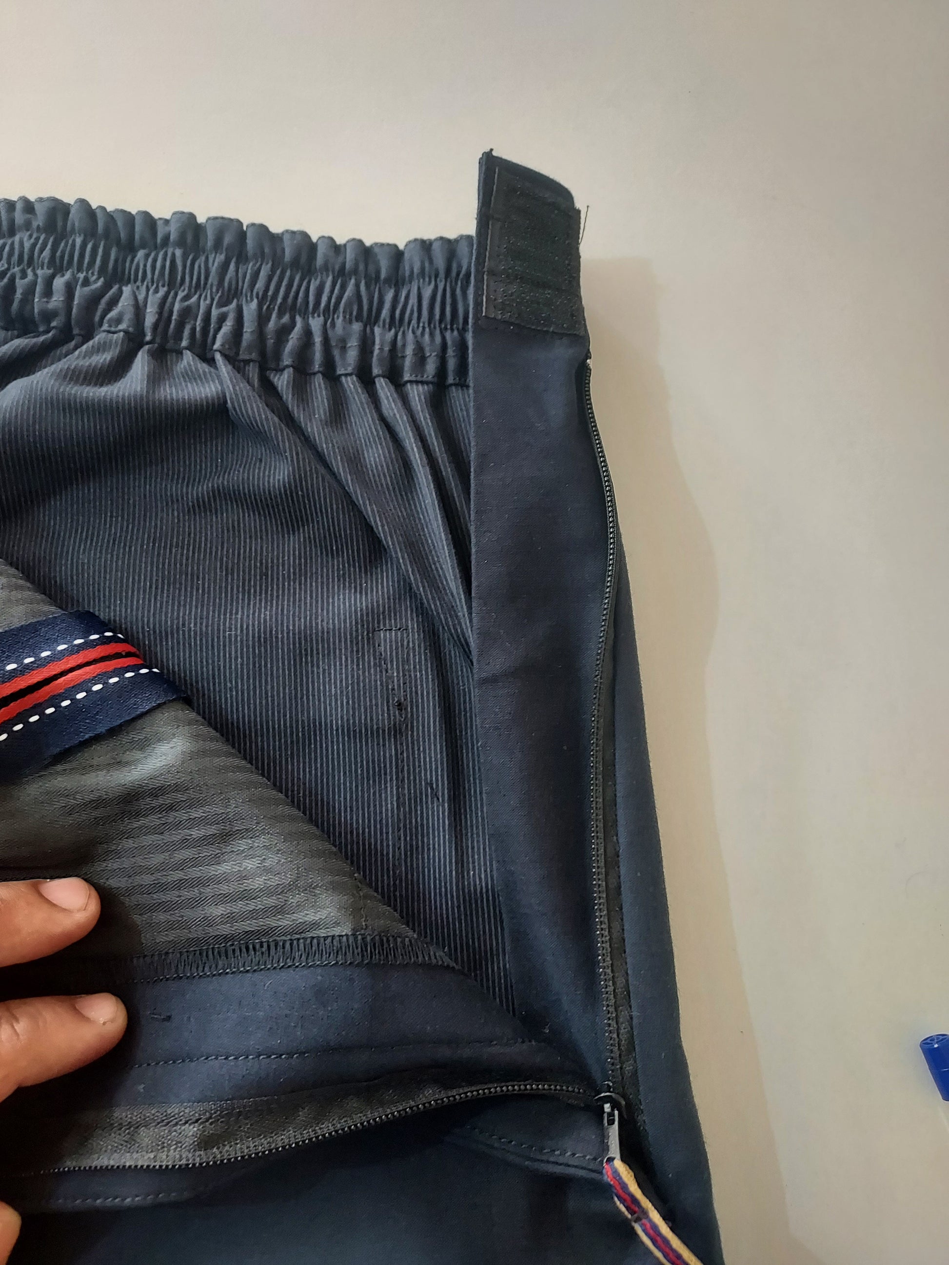Zipper is open and visible on the wearer's left. The velcro is visible on the waist band. The pulling tape to assist the wearer and caregiver is visible. 